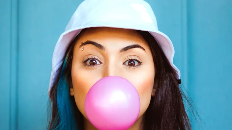 Pembe sakız balonu şişiren şapkalı genç bir kadın